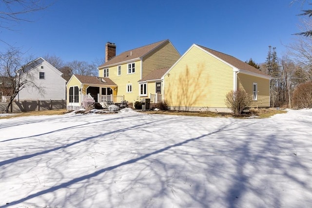 snow covered back of property featuring a sunroom and a chimney