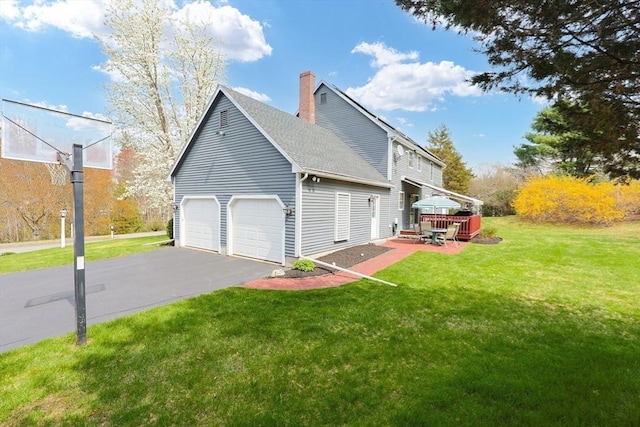 view of side of property featuring a shingled roof, aphalt driveway, a garage, a chimney, and a lawn