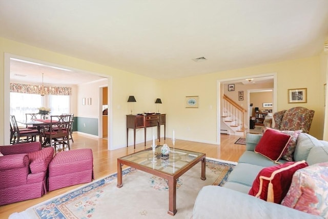 living area featuring visible vents, an inviting chandelier, baseboards, stairway, and light wood-type flooring