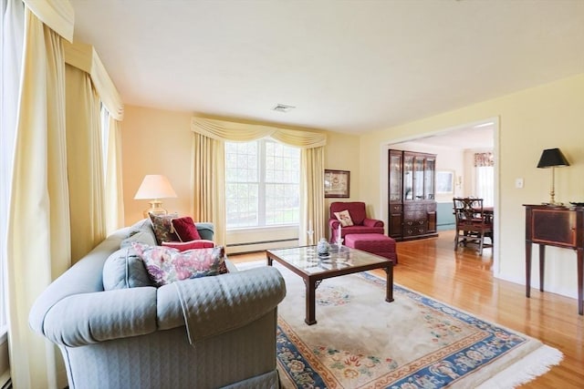 living room with a healthy amount of sunlight, a baseboard heating unit, wood finished floors, and visible vents