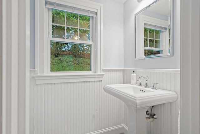 bathroom with wainscoting, a sink, and a decorative wall
