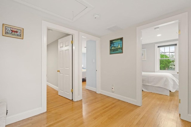 unfurnished bedroom with attic access, light wood finished floors, and baseboards