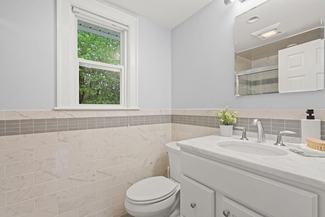 bathroom featuring tile walls, toilet, a shower stall, vanity, and wainscoting