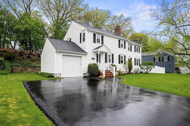 colonial house featuring a chimney, driveway, an attached garage, and a front yard