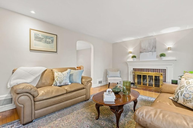 living area with arched walkways, wood finished floors, a brick fireplace, baseboards, and recessed lighting