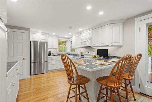 kitchen with white appliances, a peninsula, white cabinetry, a breakfast bar area, and recessed lighting