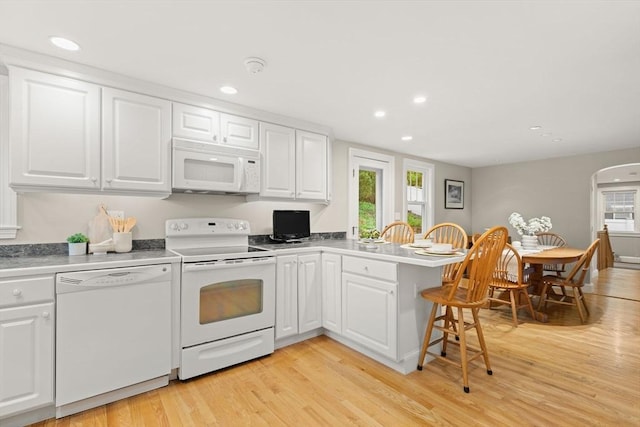 kitchen with white appliances, plenty of natural light, a peninsula, white cabinets, and recessed lighting