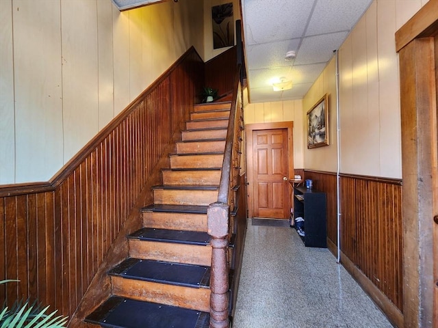 staircase with a paneled ceiling, wood walls, and wainscoting