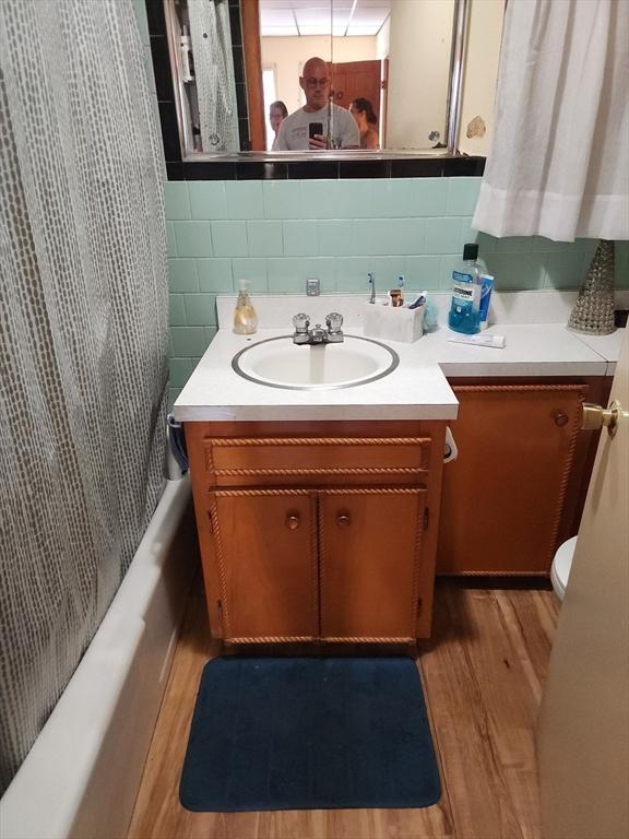 full bathroom featuring vanity, wood finished floors, decorative backsplash, shower / bath combination with curtain, and tile walls