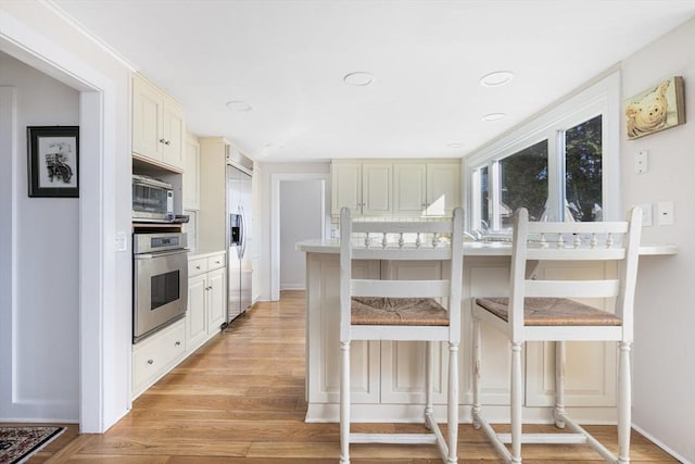 kitchen with light hardwood / wood-style floors, a kitchen bar, and appliances with stainless steel finishes