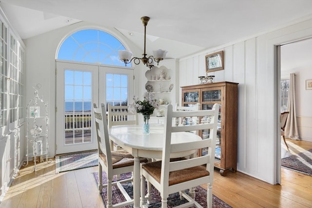 dining area with french doors, vaulted ceiling, a water view, an inviting chandelier, and light hardwood / wood-style flooring