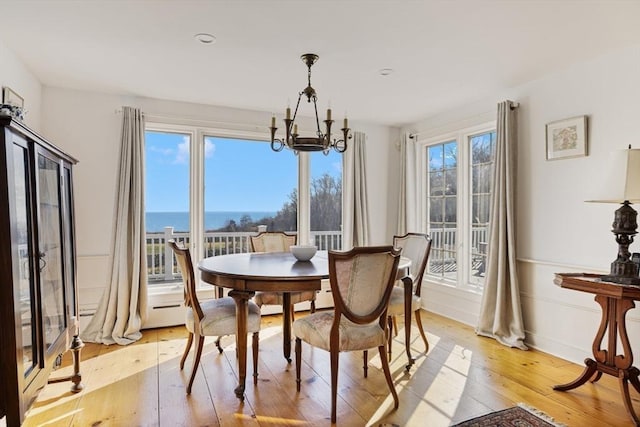 dining area with an inviting chandelier, a water view, and light wood-type flooring