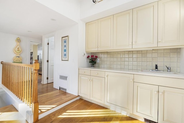 kitchen with backsplash, radiator, sink, built in refrigerator, and light hardwood / wood-style flooring