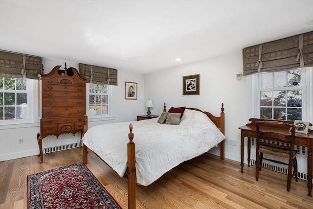 bedroom featuring wood-type flooring, radiator heating unit, and multiple windows