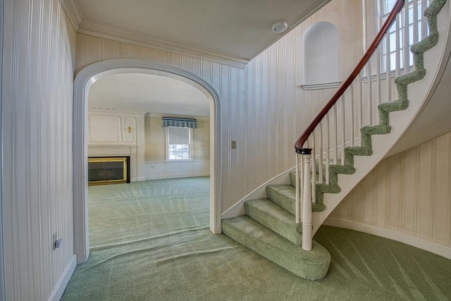 stairs with carpet, a fireplace, arched walkways, and ornamental molding