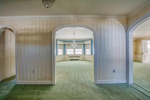 carpeted empty room featuring ornamental molding, arched walkways, a notable chandelier, and radiator heating unit