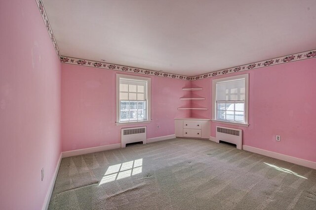 carpeted empty room featuring baseboards and radiator heating unit