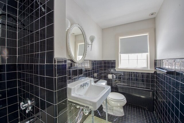 bathroom with tile walls, toilet, wainscoting, a sink, and tile patterned flooring