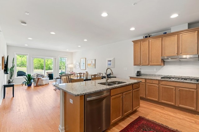 kitchen featuring stainless steel appliances, a sink, under cabinet range hood, a kitchen island with sink, and light stone countertops
