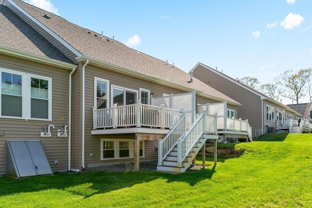 rear view of property with a wooden deck, a lawn, and roof with shingles