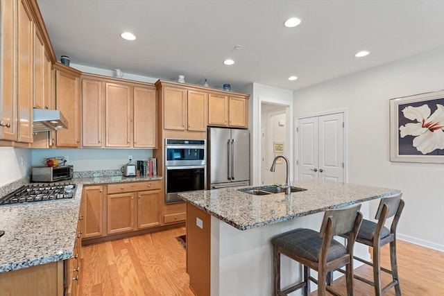 kitchen featuring a sink, stainless steel appliances, under cabinet range hood, light wood-style flooring, and recessed lighting