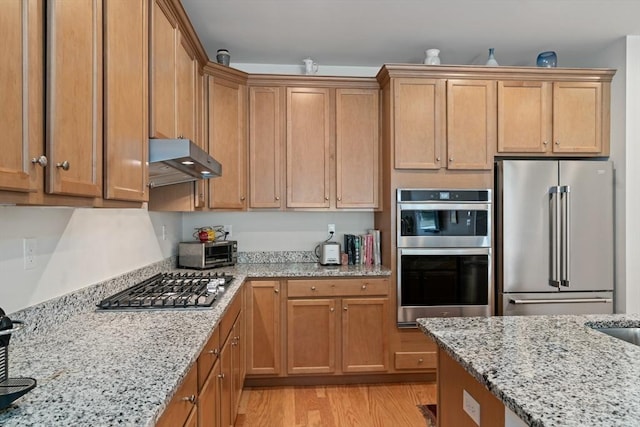 kitchen featuring appliances with stainless steel finishes, under cabinet range hood, light wood-style floors, and light stone countertops