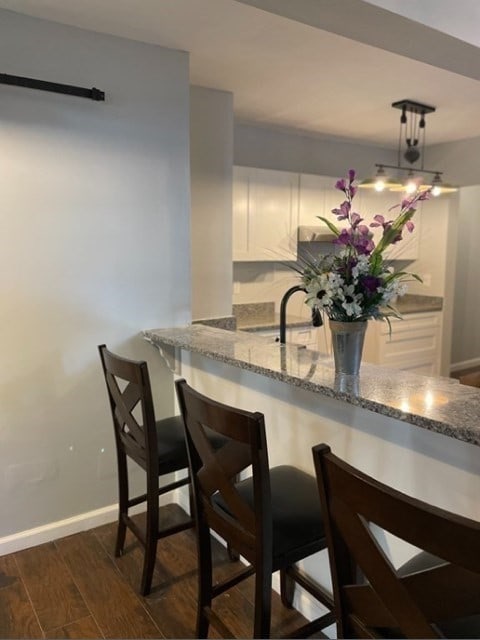 kitchen featuring dark hardwood / wood-style flooring, light stone counters, sink, a breakfast bar area, and white cabinetry