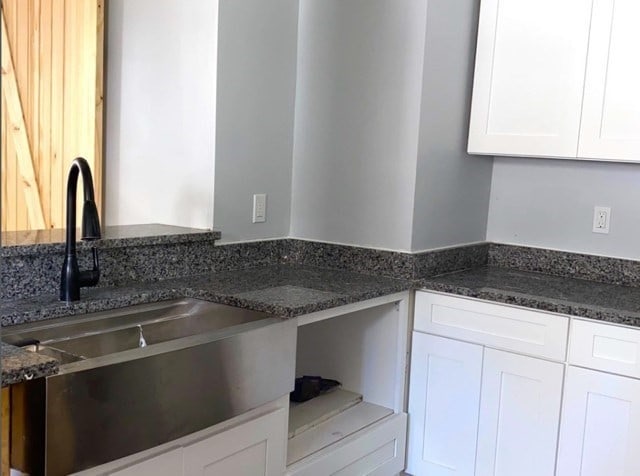 kitchen featuring white cabinetry, dark stone counters, and sink