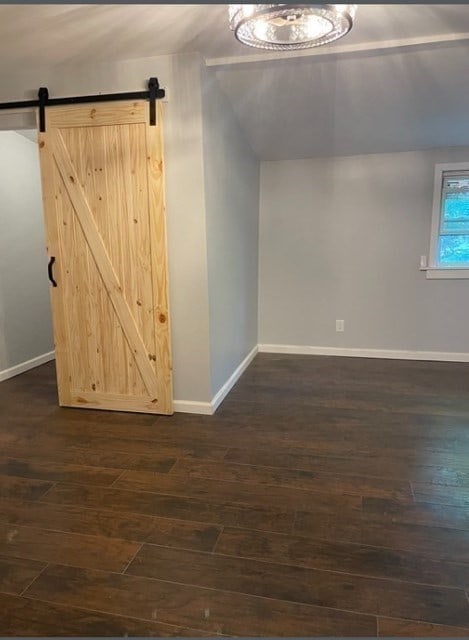 unfurnished room featuring vaulted ceiling, a barn door, and dark hardwood / wood-style floors