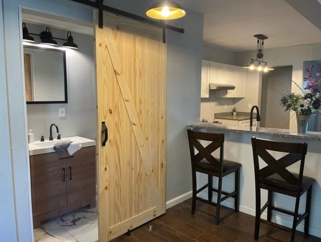 kitchen featuring wall chimney range hood, hanging light fixtures, hardwood / wood-style floors, white cabinetry, and sink