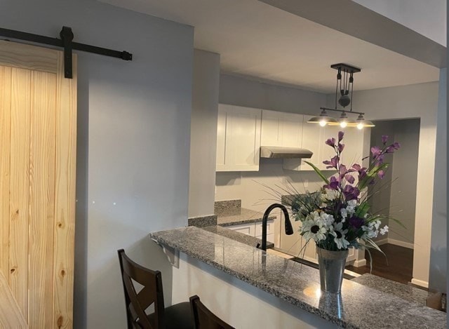 kitchen with white cabinets, dark stone counters, a barn door, and hardwood / wood-style flooring