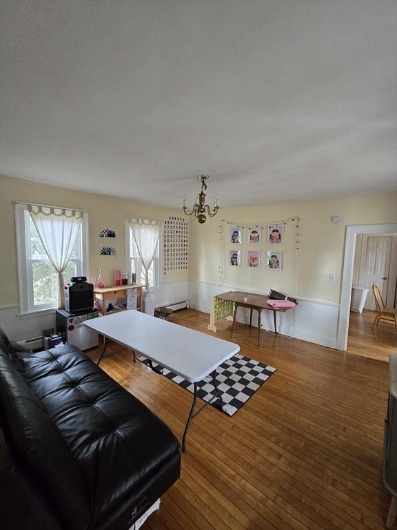 dining room featuring a chandelier, healthy amount of natural light, wood finished floors, and a baseboard heating unit