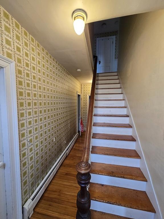 staircase with a baseboard heating unit, wood finished floors, and wallpapered walls