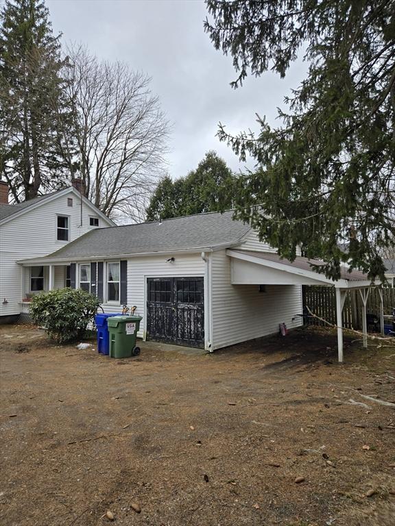 view of side of home with an attached garage, a chimney, driveway, and a shingled roof