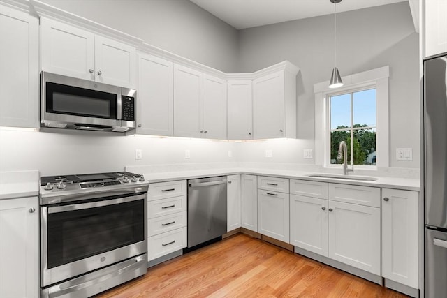 kitchen with stainless steel appliances, sink, decorative light fixtures, light hardwood / wood-style floors, and white cabinetry