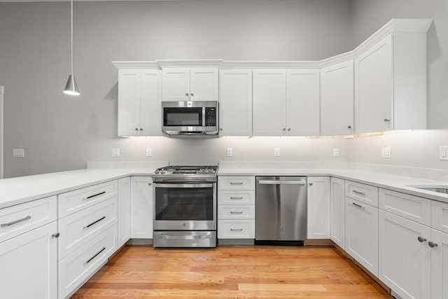 kitchen with pendant lighting, white cabinetry, stainless steel appliances, and light hardwood / wood-style flooring