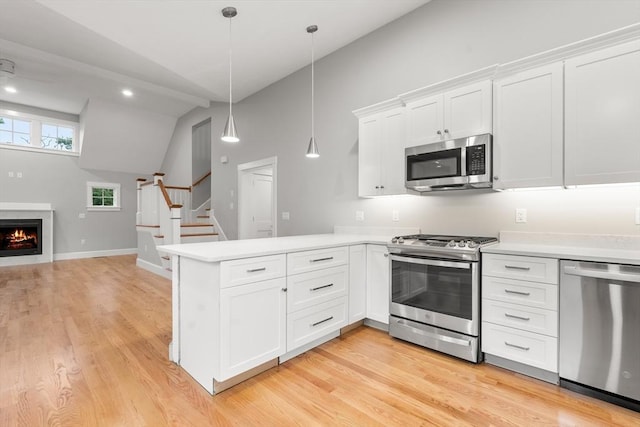 kitchen featuring kitchen peninsula, appliances with stainless steel finishes, vaulted ceiling, decorative light fixtures, and white cabinets