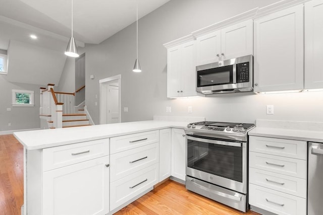 kitchen with kitchen peninsula, vaulted ceiling, appliances with stainless steel finishes, decorative light fixtures, and white cabinetry