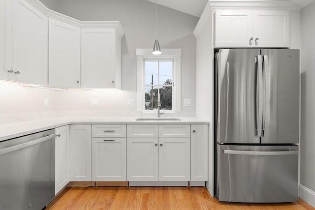 kitchen featuring white cabinets, hanging light fixtures, sink, light wood-type flooring, and appliances with stainless steel finishes