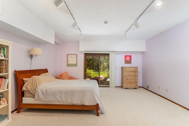 carpeted bedroom with baseboards, rail lighting, and access to exterior
