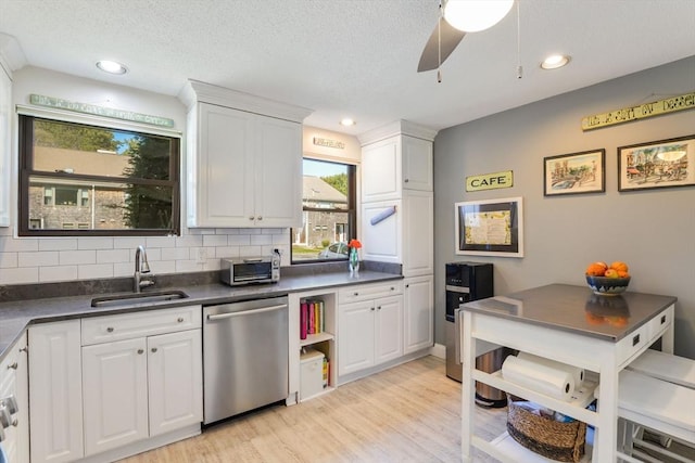 kitchen with dark countertops, tasteful backsplash, stainless steel dishwasher, light wood-type flooring, and a sink