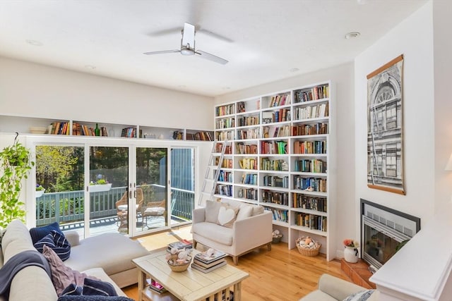 sitting room with a ceiling fan, a glass covered fireplace, and wood finished floors