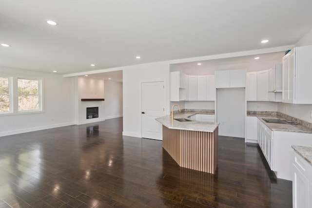 kitchen with sink, white cabinetry, light stone counters, an island with sink, and dark hardwood / wood-style flooring