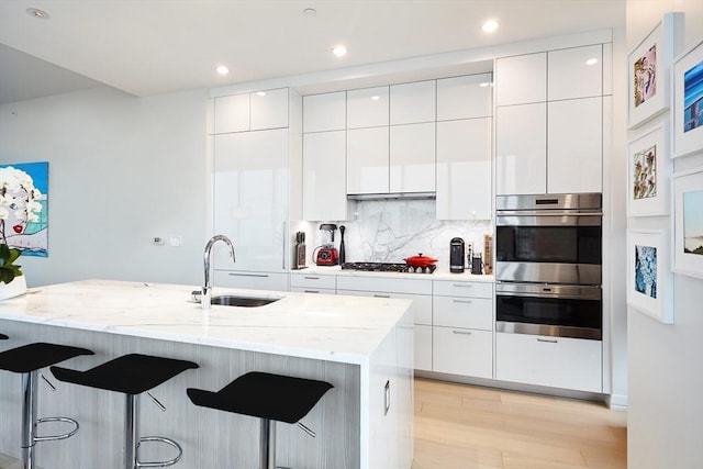 kitchen with a kitchen bar, appliances with stainless steel finishes, decorative backsplash, sink, and white cabinets