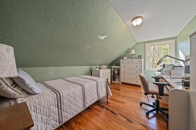 bedroom featuring a textured ceiling, light hardwood / wood-style flooring, and lofted ceiling