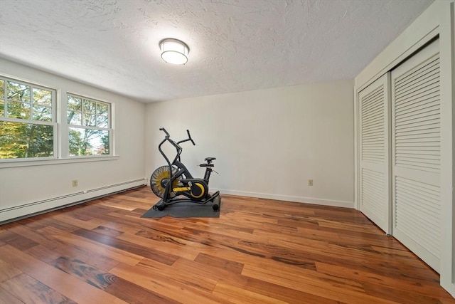 workout room with hardwood / wood-style floors, a textured ceiling, and a baseboard heating unit