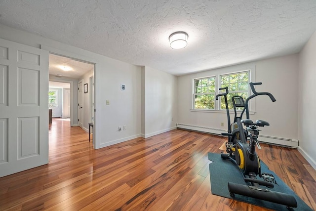 exercise area with wood-type flooring, a textured ceiling, and a baseboard heating unit