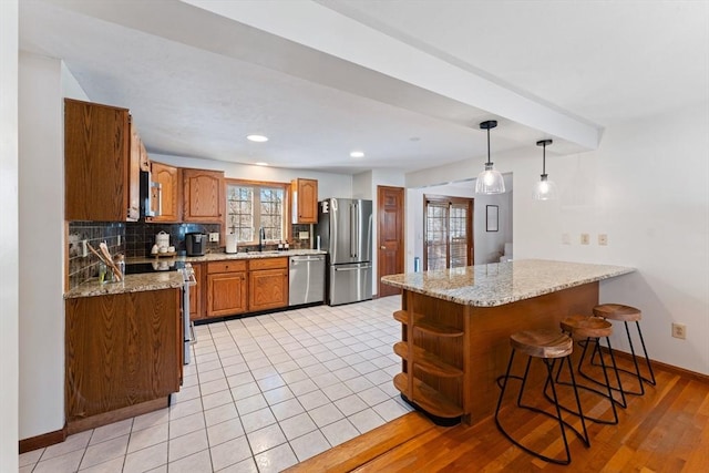 kitchen featuring light stone counters, hanging light fixtures, kitchen peninsula, stainless steel appliances, and backsplash