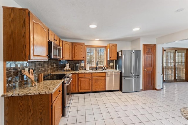 kitchen with sink, light tile patterned floors, appliances with stainless steel finishes, light stone countertops, and decorative backsplash