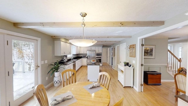 dining space with sink, beam ceiling, and light hardwood / wood-style flooring